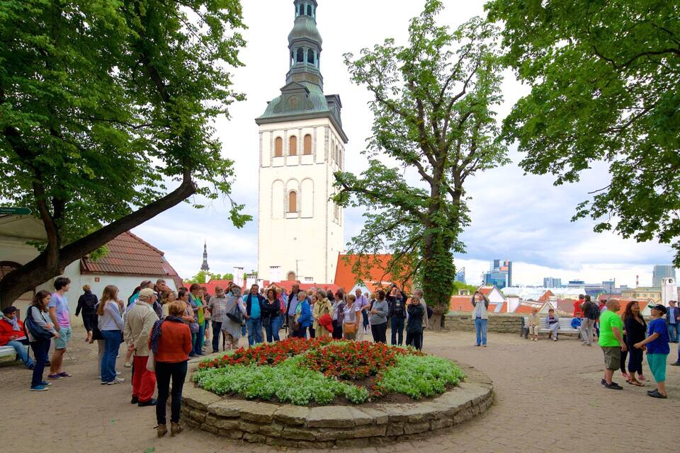 A historic church with a tall tower, surrounded by a crowd of people and a flower bed in the foreground.