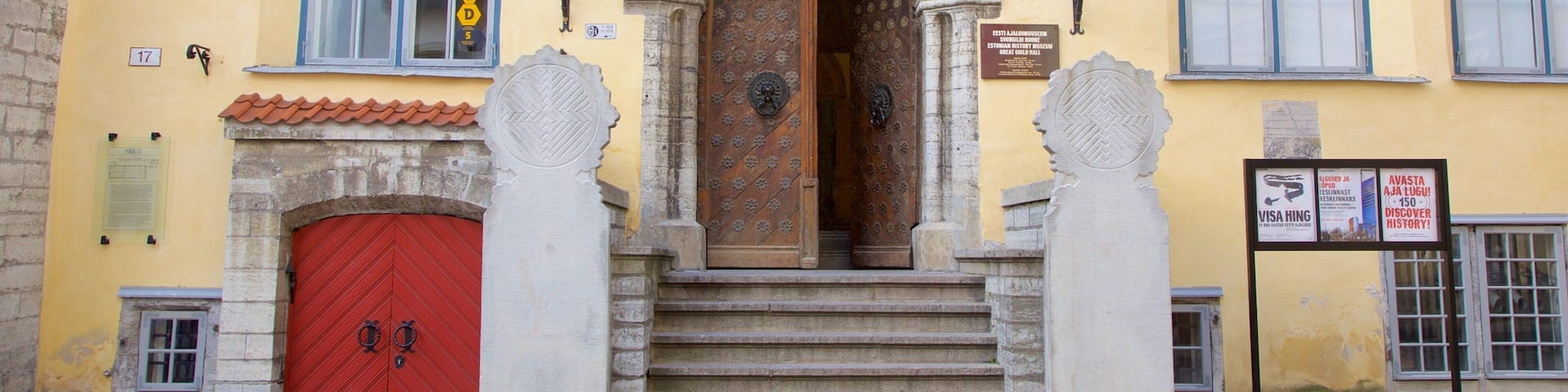 A yellow building with a red door, two arched windows, and a stone staircase leading to the entrance.
