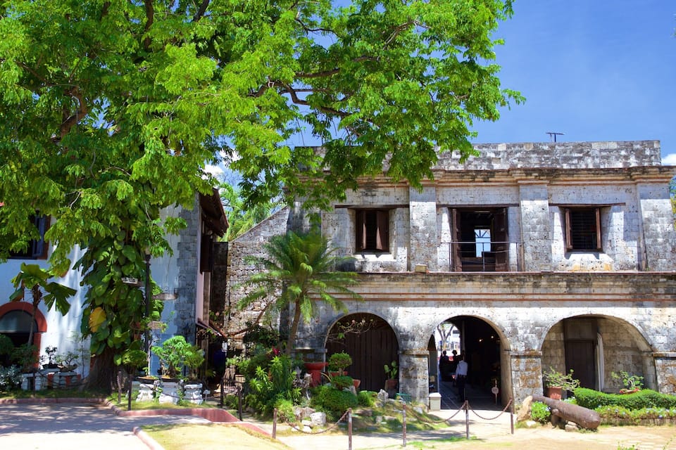 A historic stone building with arched doorways and a garden in front.