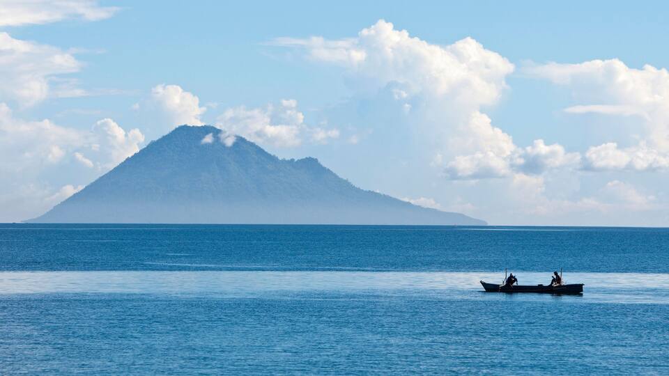 A calm sea with a boat and a mountain in the distance.