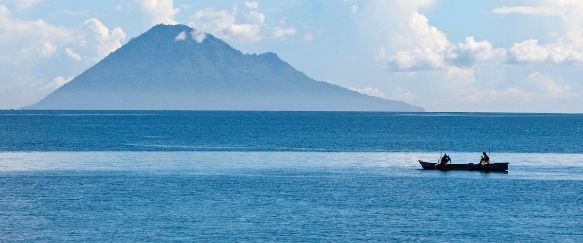 A calm sea with a boat and a mountain in the distance.