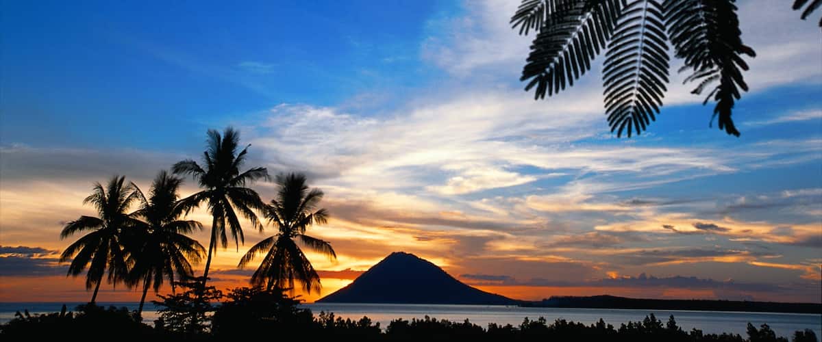 A sunset over a volcano with palm trees silhouetted against the sky.