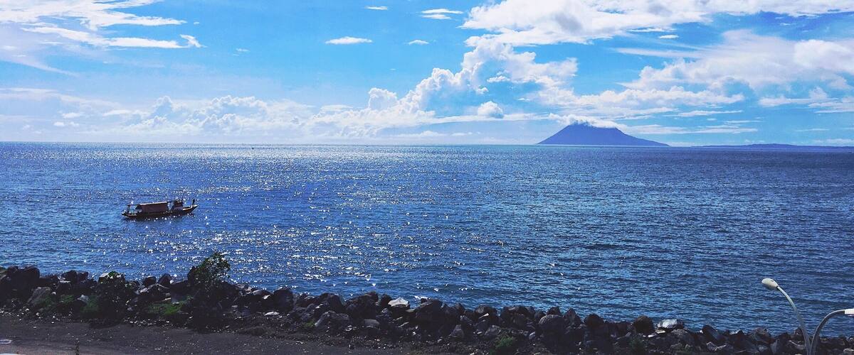 A calm sea with a boat, rocky shoreline, and a distant mountain.