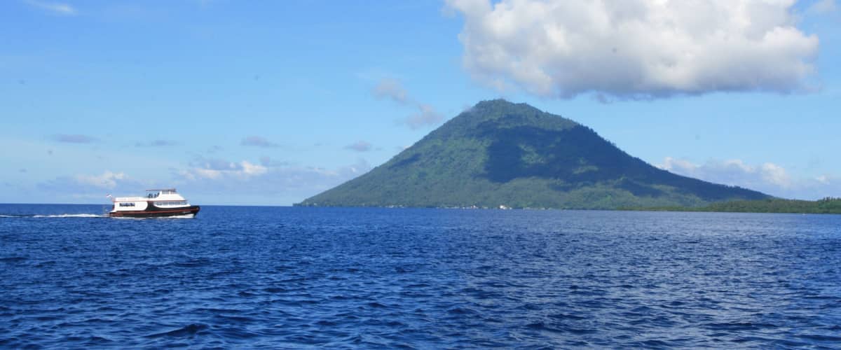 A boat on a calm sea with a green mountain in the background.