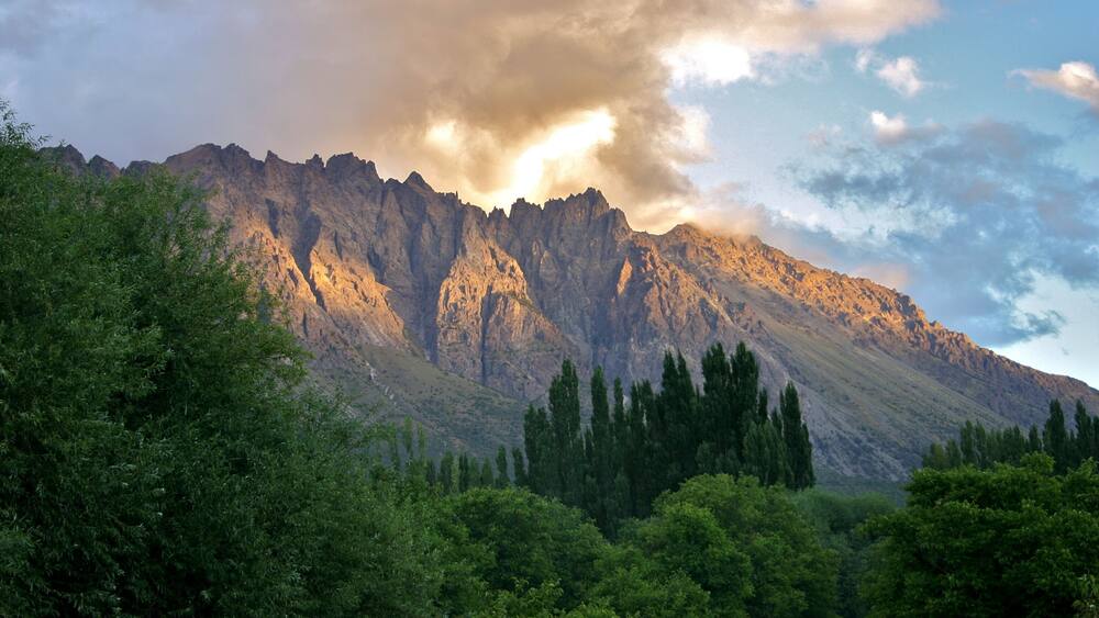 A mountain range with dense green forests in the foreground and a clear sky.
