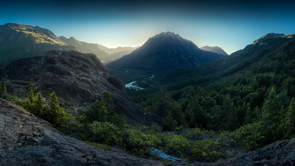 A mountainous landscape with a valley, dense forest, and a river.