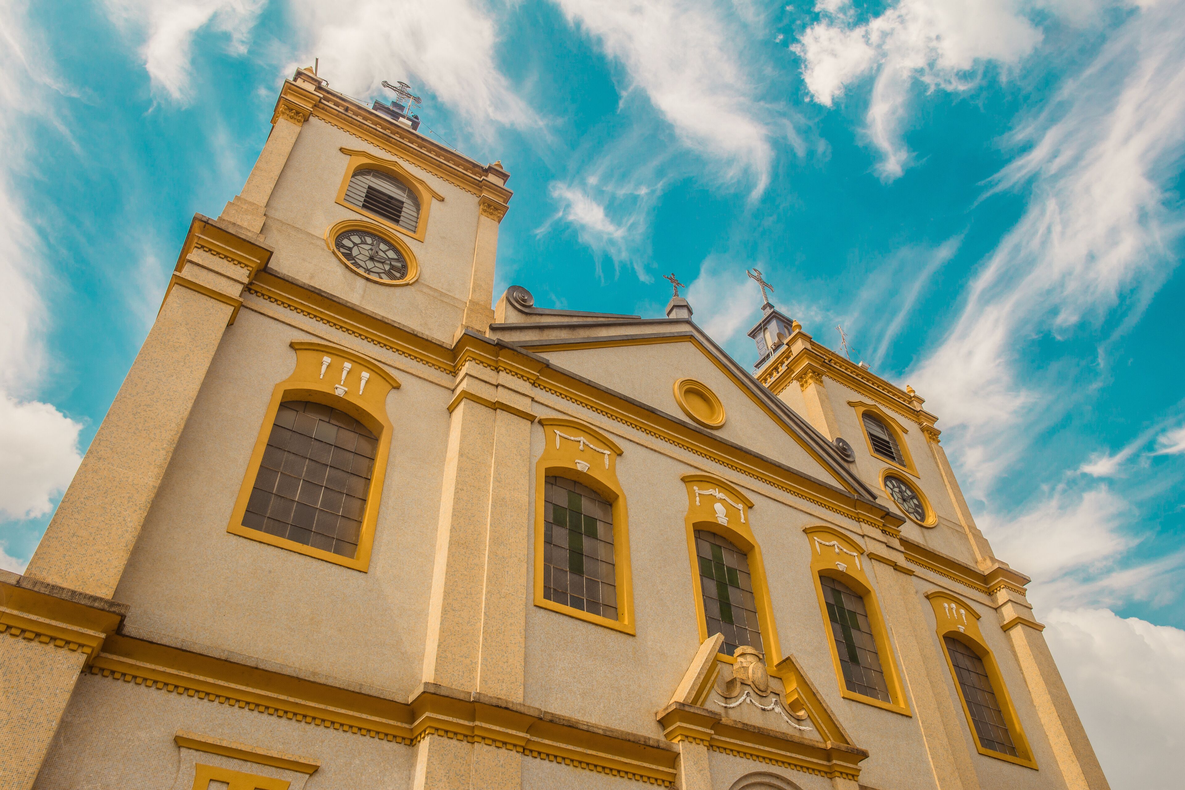A church with a clock tower and a cross on top, under a blue sky with clouds.