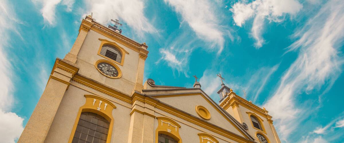 A church with a clock tower and a cross on top, under a blue sky with clouds.
