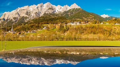 Una catena montuosa con un lago che riflette il paesaggio circostante, comprendente case e una chiesa.