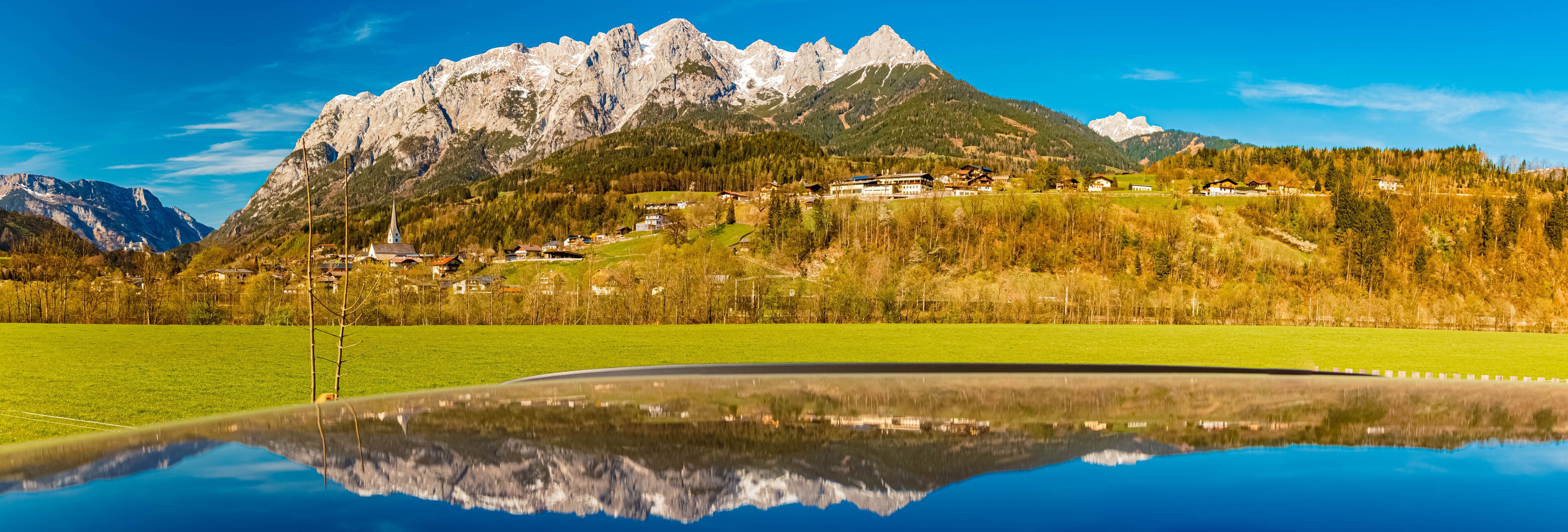 A mountain range with a lake reflecting the scenery, including houses and a church.
