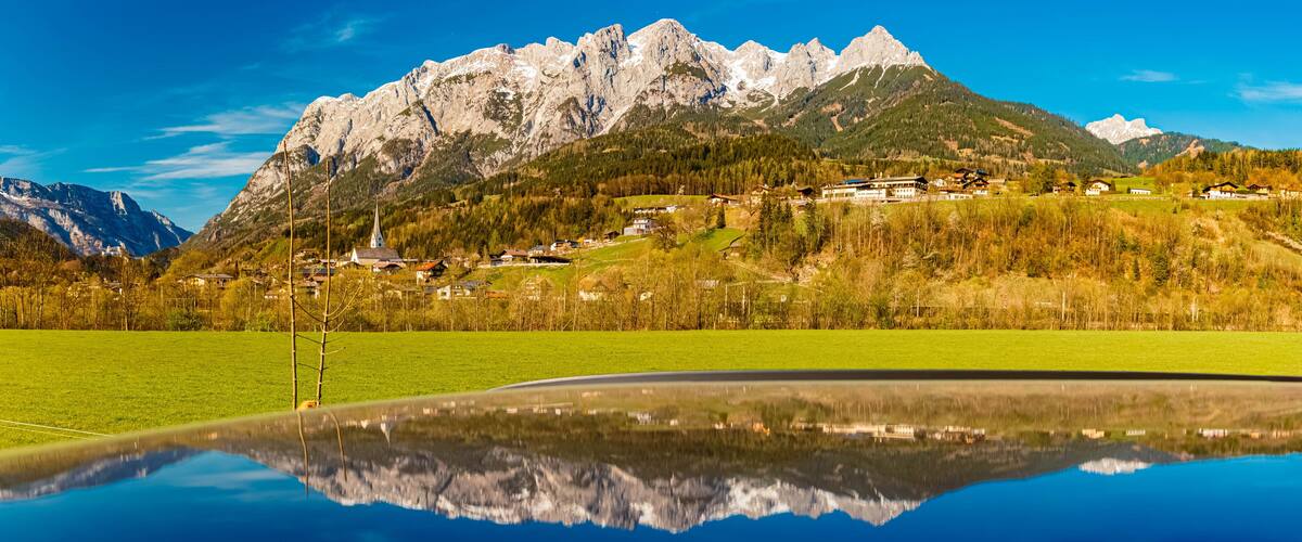 A mountain range with a lake reflecting the scenery, including houses and a church.