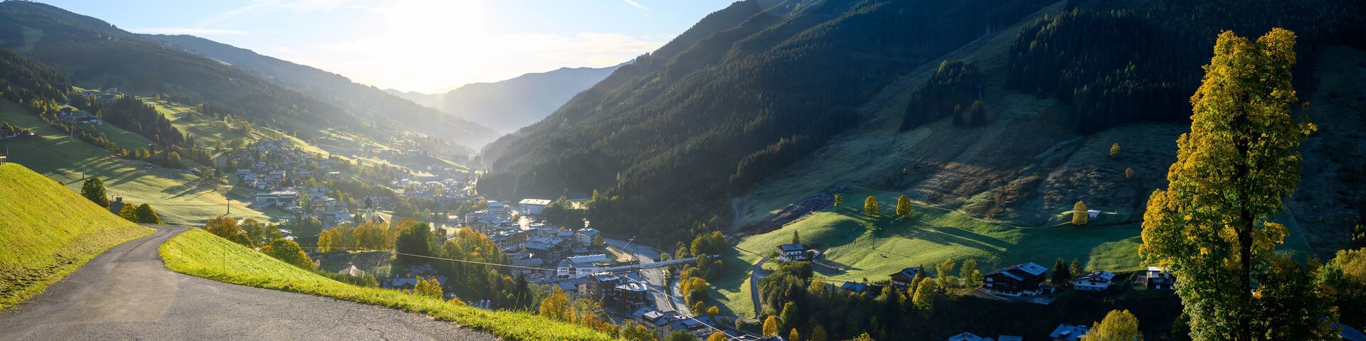 Um vale com uma estrada sinuosa, casas e montanhas ao fundo.