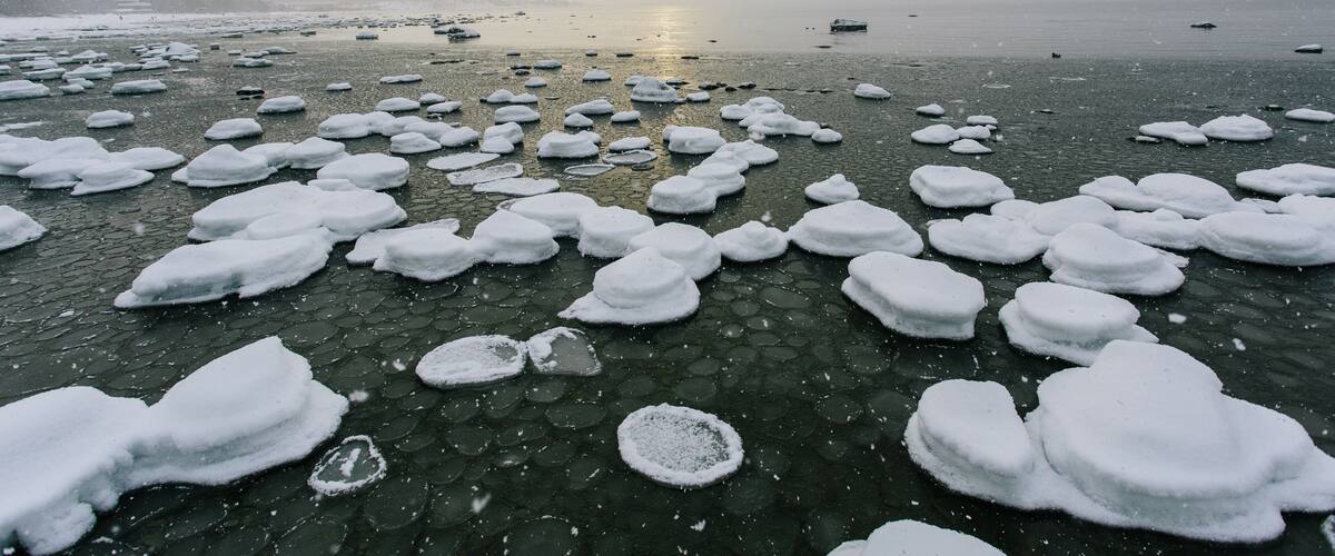 A snowy beach with ice formations and a distant sun.