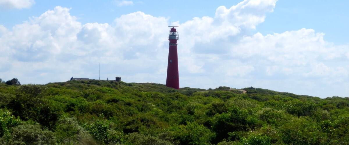A red lighthouse on a hill with green vegetation and a partly cloudy sky.