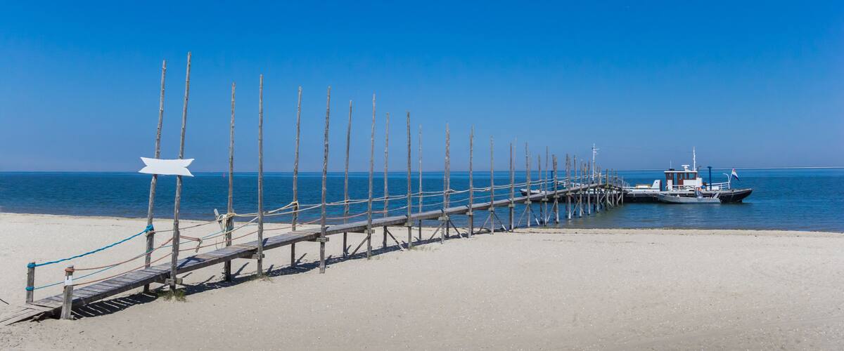 A wooden pier extending into calm waters, a clear blue sky, and a boat anchored near the end.