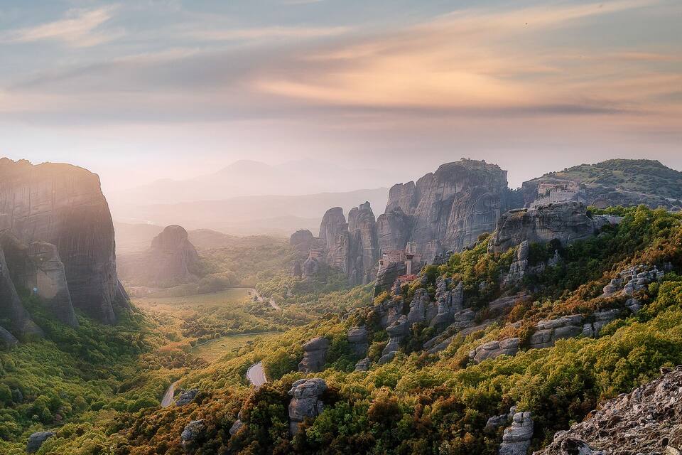A canyon with towering rock formations and a winding road through a lush valley.