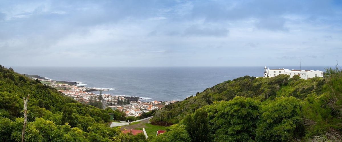 A coastal town with white buildings, a lighthouse, and lush greenery.