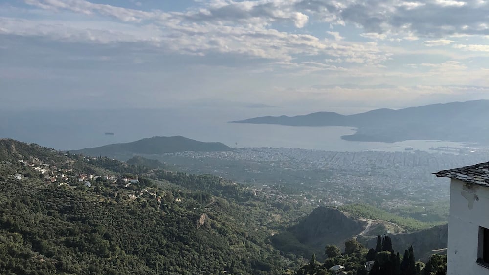 A coastal landscape with a view of the sea, hills, and scattered buildings.