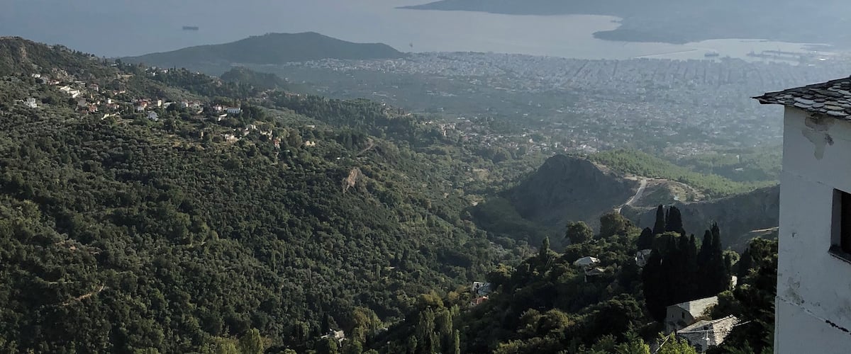 A coastal landscape with a view of the sea, hills, and scattered buildings.
