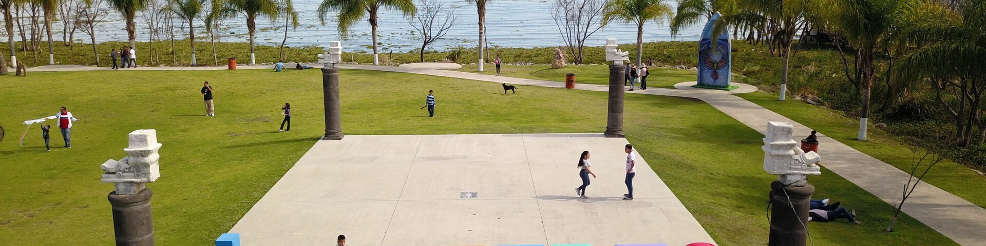 Un parque con un gran cartel de 'JOCOTEC', palmeras y vista al mar y las montañas al fondo.