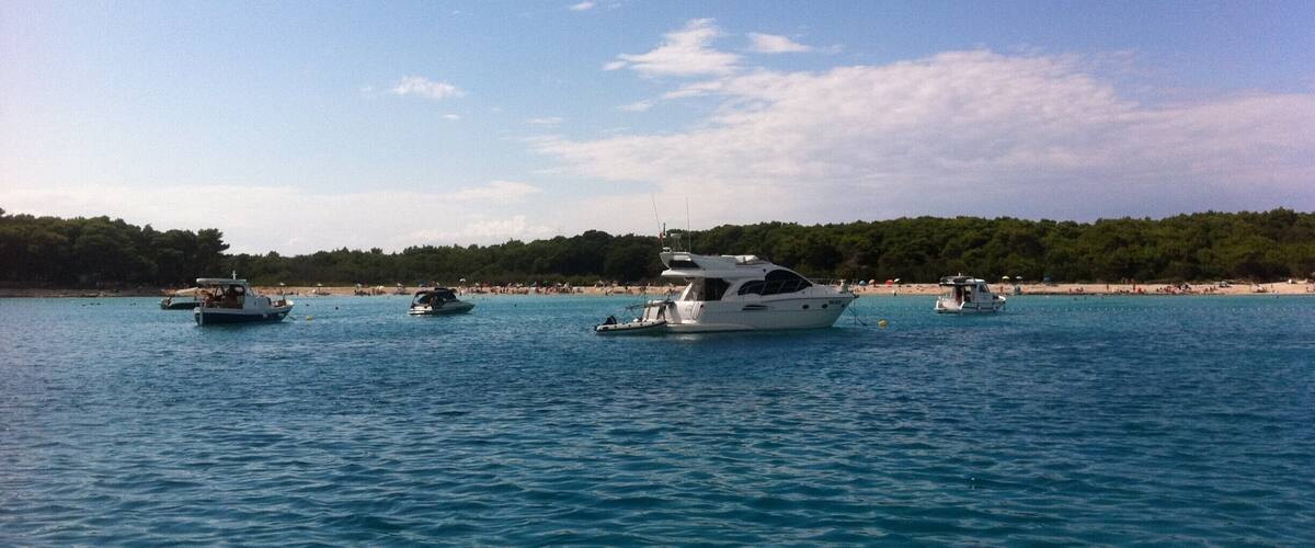 A calm sea with several boats anchored near a beach.