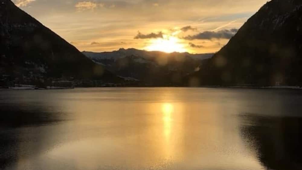 Ein ruhiger See mit Bergen an beiden Seiten und der untergehenden Sonne im Hintergrund.