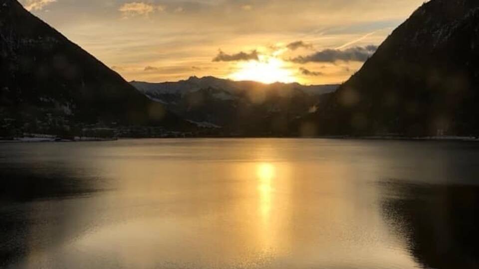 A calm lake with mountains on either side and the sun setting in the background.