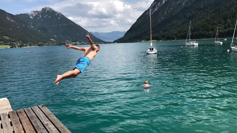 A man diving into a lake surrounded by mountains and boats.