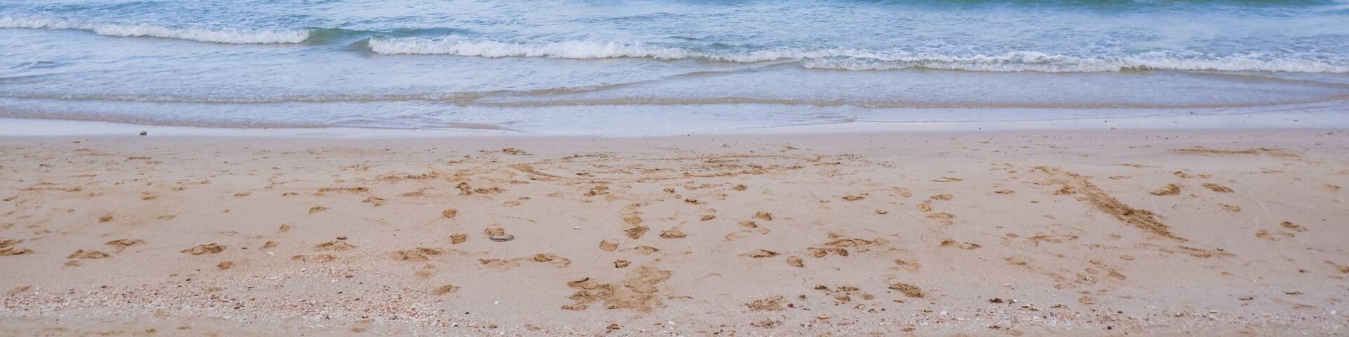 A beach with clear blue water and a sandy shore.