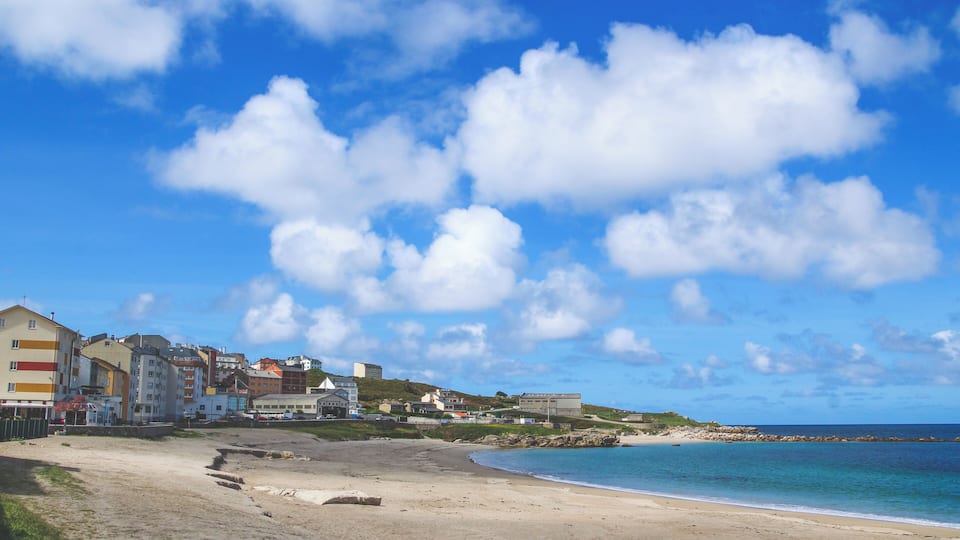 A beach with buildings in the background and a clear blue sky.