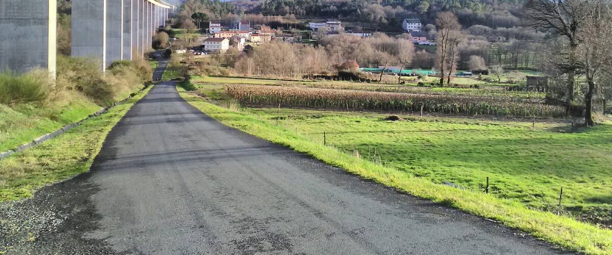 A rural road under a bridge, surrounded by fields and houses.