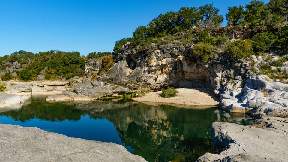 A clear lake surrounded by rocky terrain and dense greenery.