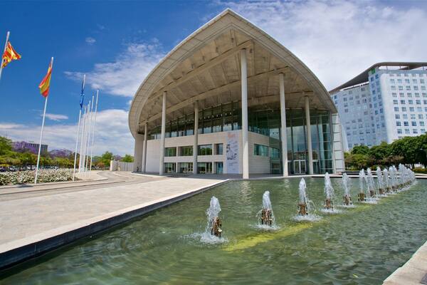A modern building with a unique curved roof and a fountain in front.