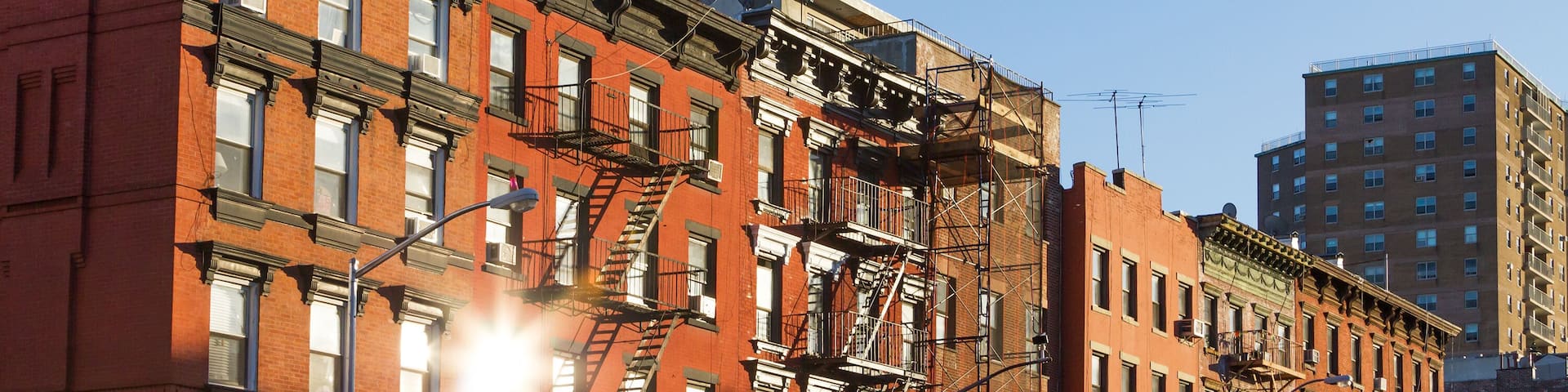 A street sign for St Marks Pl, a red brick building with multiple windows and fire escapes, and a taller building in the background.