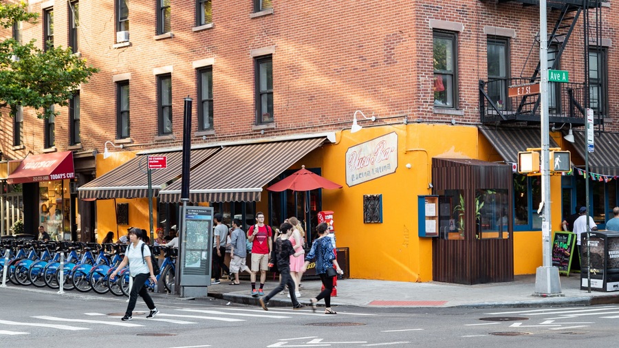 A busy street corner with a yellow building, a red awning, and a sign for 'Pura Vida Cocina Latina'.