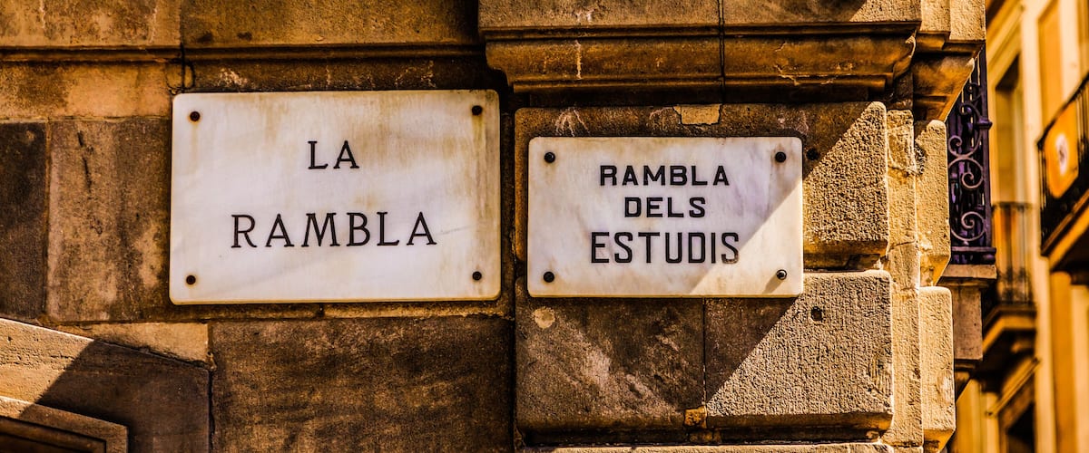 Two street signs on a building wall, one reads "LA RAMBLA" and the other "RAMBLA DELS ESTUDIS".
