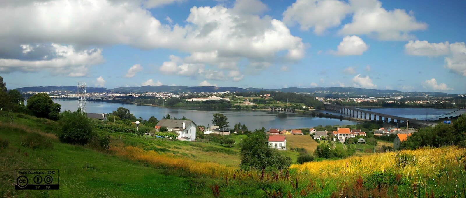 A river with a bridge, houses, and a hilly landscape.