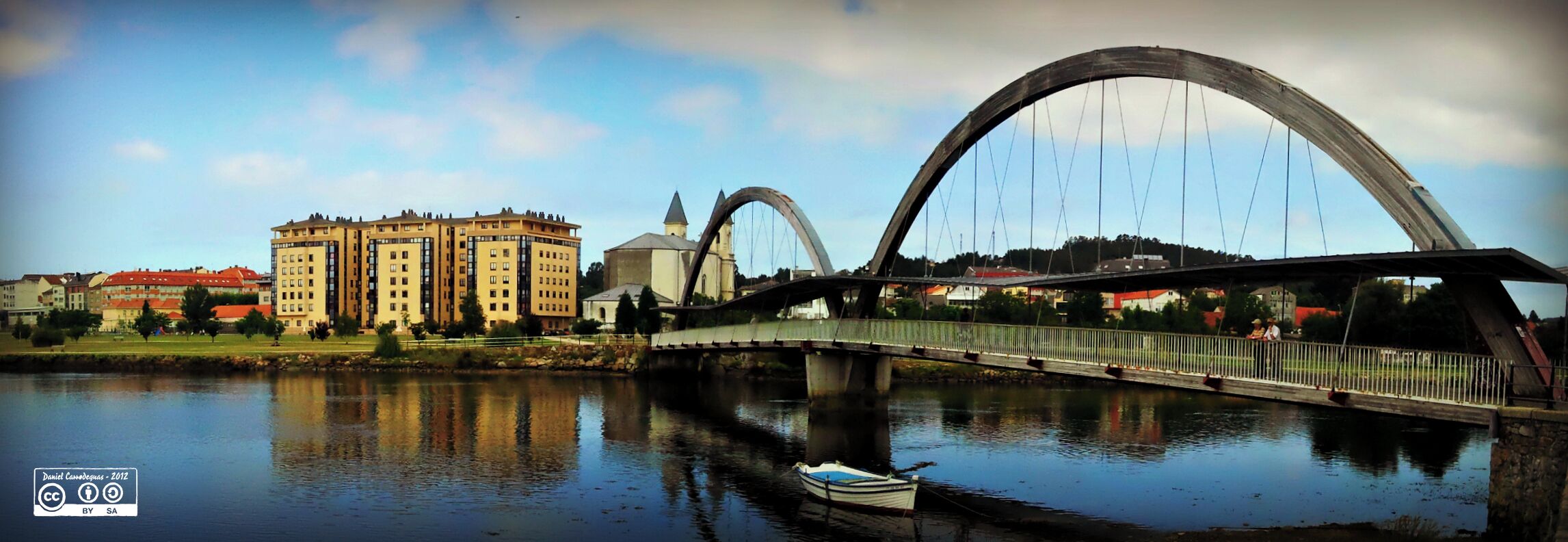 A river with a bridge, a boat, and buildings including a church.
