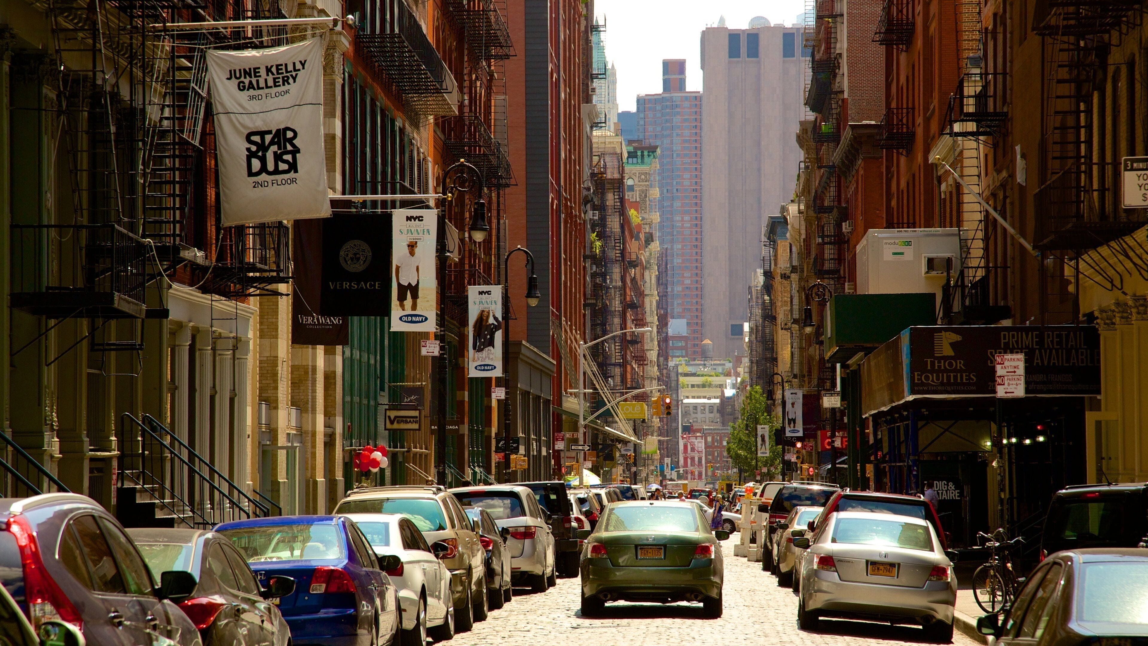 Una concurrida calle urbana bordeada de vehículos estacionados y diversos edificios comerciales.