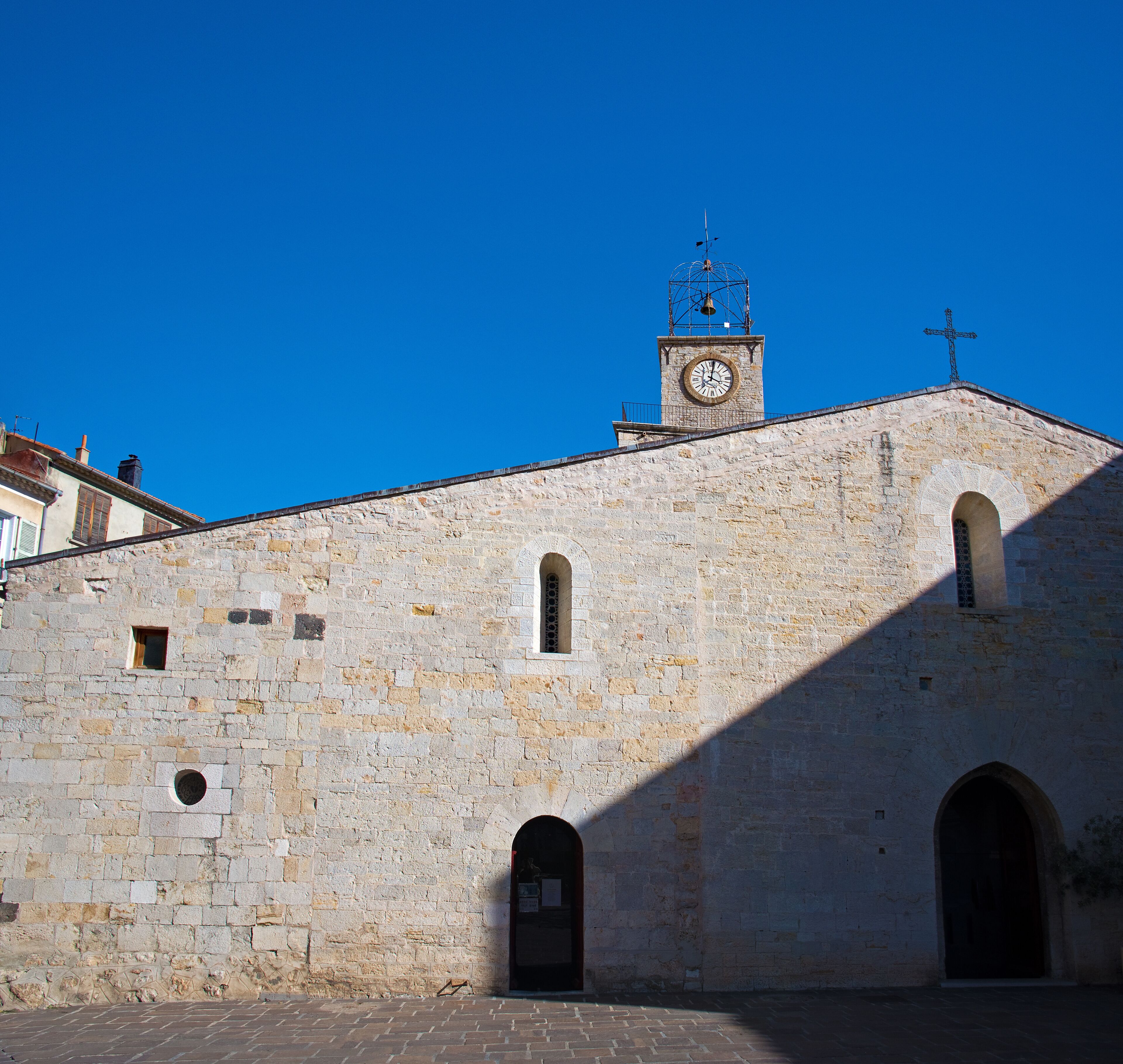 A historic stone building with a clock tower, arched doorways, and a cross on top.