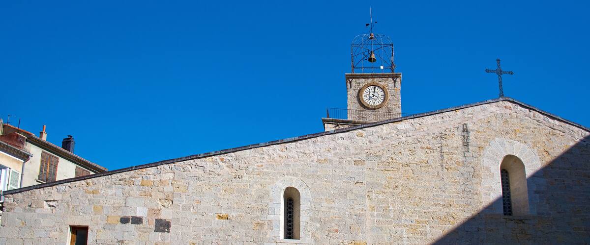 A historic stone building with a clock tower, arched doorways, and a cross on top.