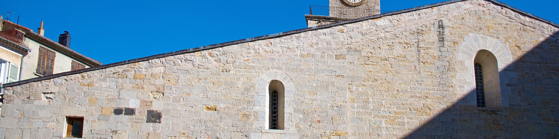 A historic stone building with a clock tower, arched doorways, and a cross on top.