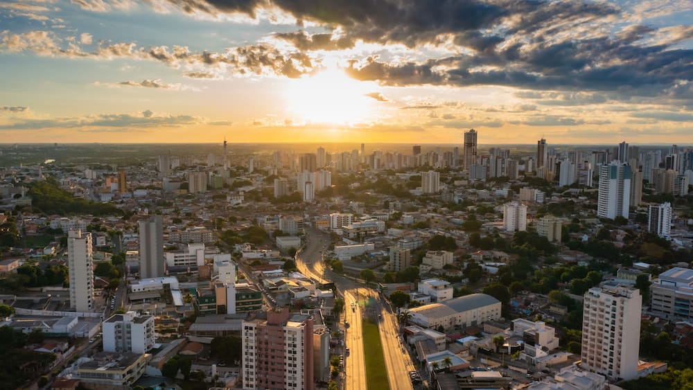 Une vue urbaine avec une rivière qui la traverse, entourée de gratte-ciel et un coucher de soleil en arrière-plan.