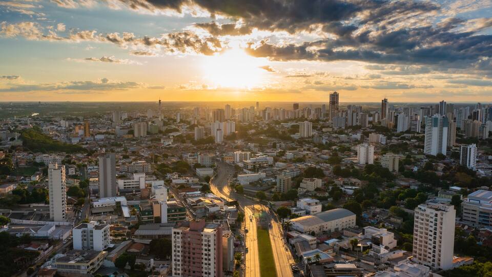 Une vue urbaine avec une rivière qui la traverse, entourée de gratte-ciel et un coucher de soleil en arrière-plan.