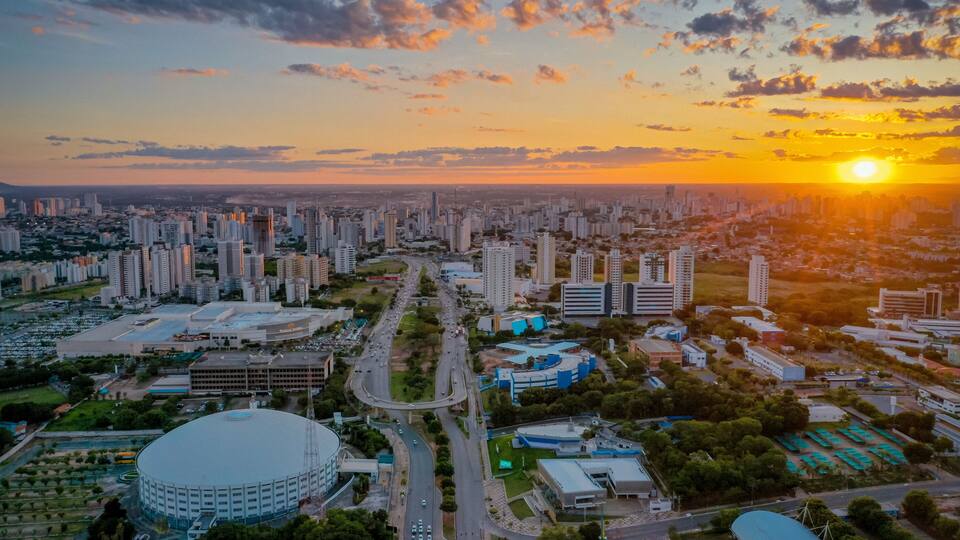 Un paisaje urbano al atardecer con rascacielos, una gran estructura circular y una red de carreteras.