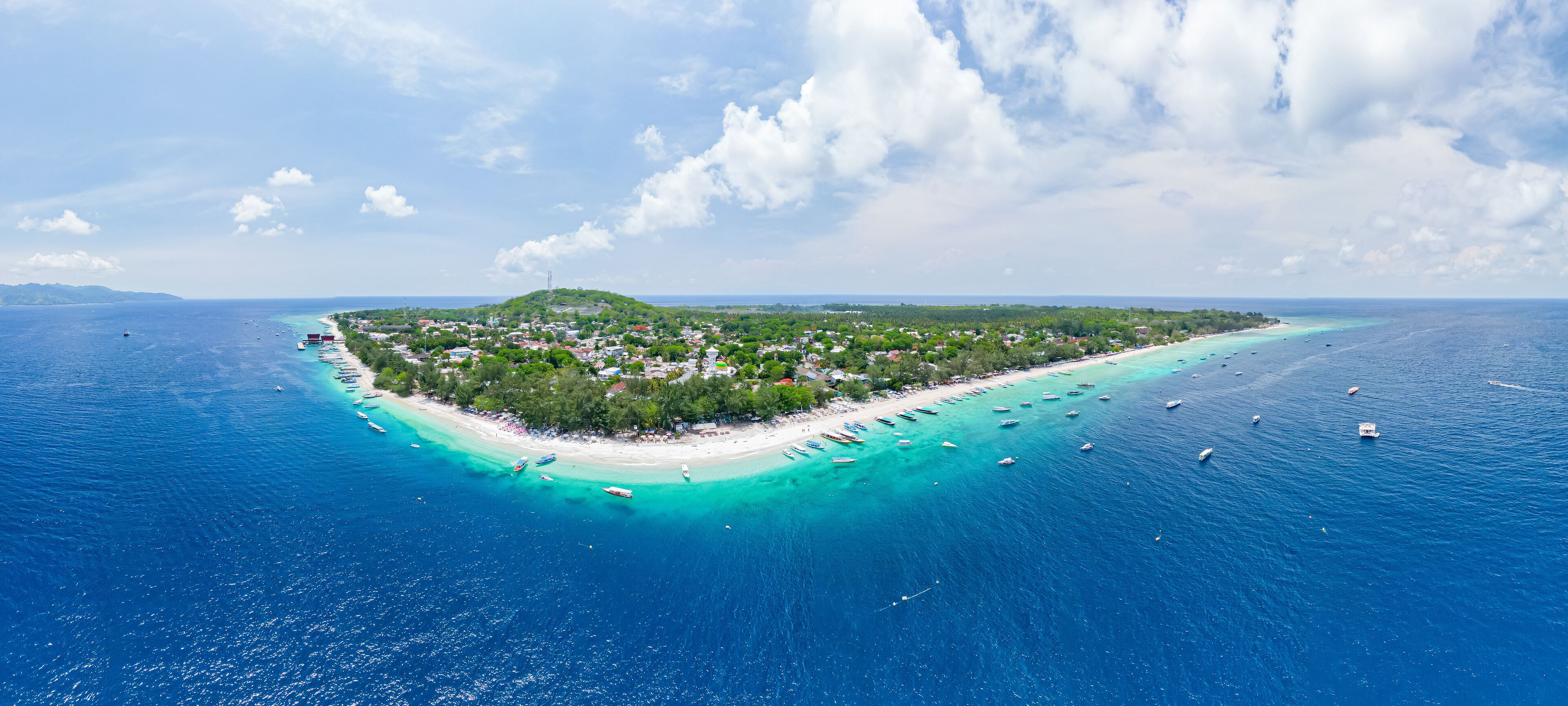 An aerial view of a tropical island with a beach, clear turquoise waters, and boats.