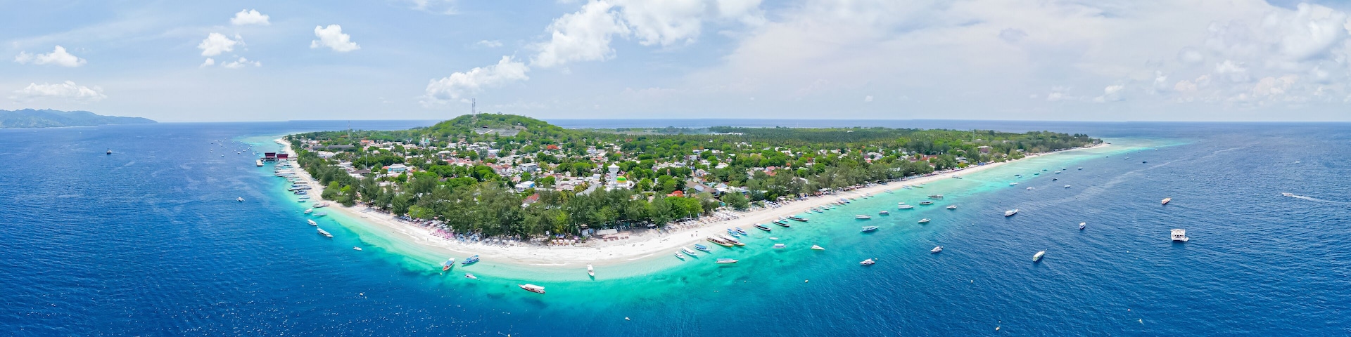 An aerial view of a tropical island with a beach, clear turquoise waters, and boats.