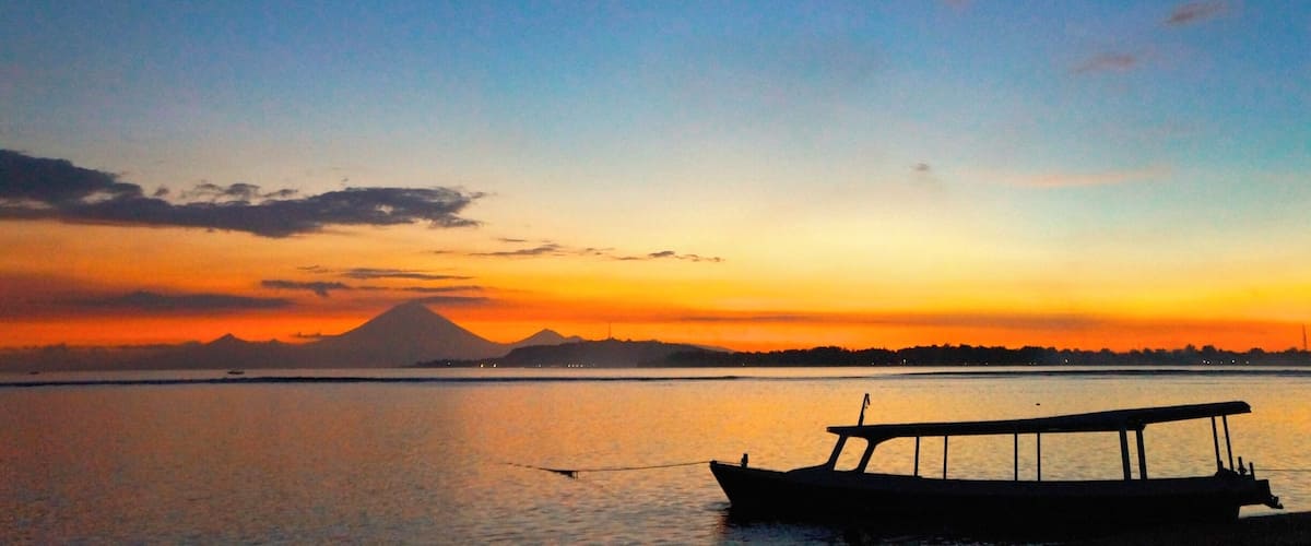 Ein Sonnenuntergang über ruhigem Gewässer mit einem Boot und einem Berg im Hintergrund.