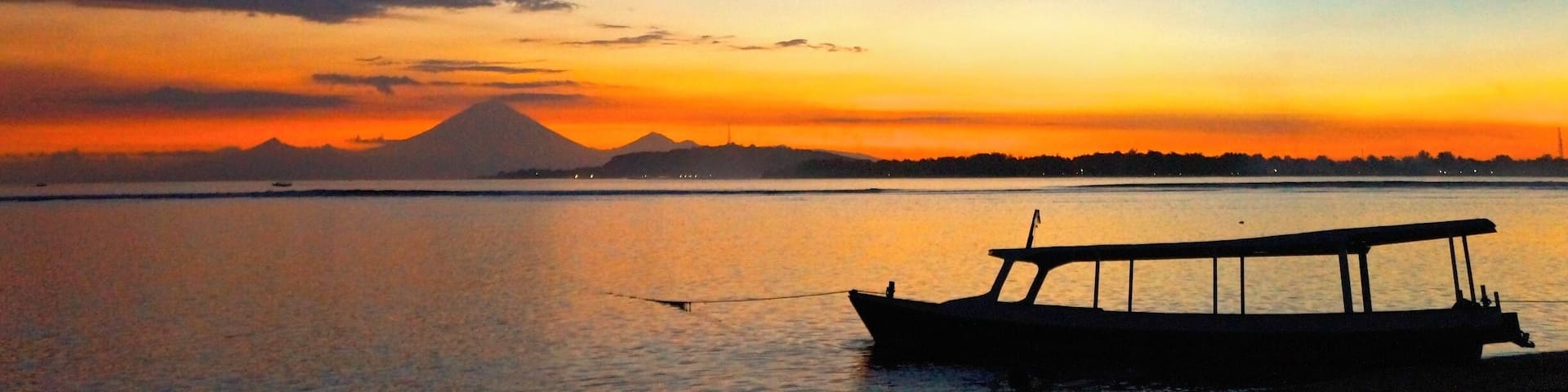 A sunset over a calm body of water with a boat and a mountain in the background.