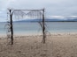 Une plage agrémentée d’une arche en bois décorée de plantes suspendues.